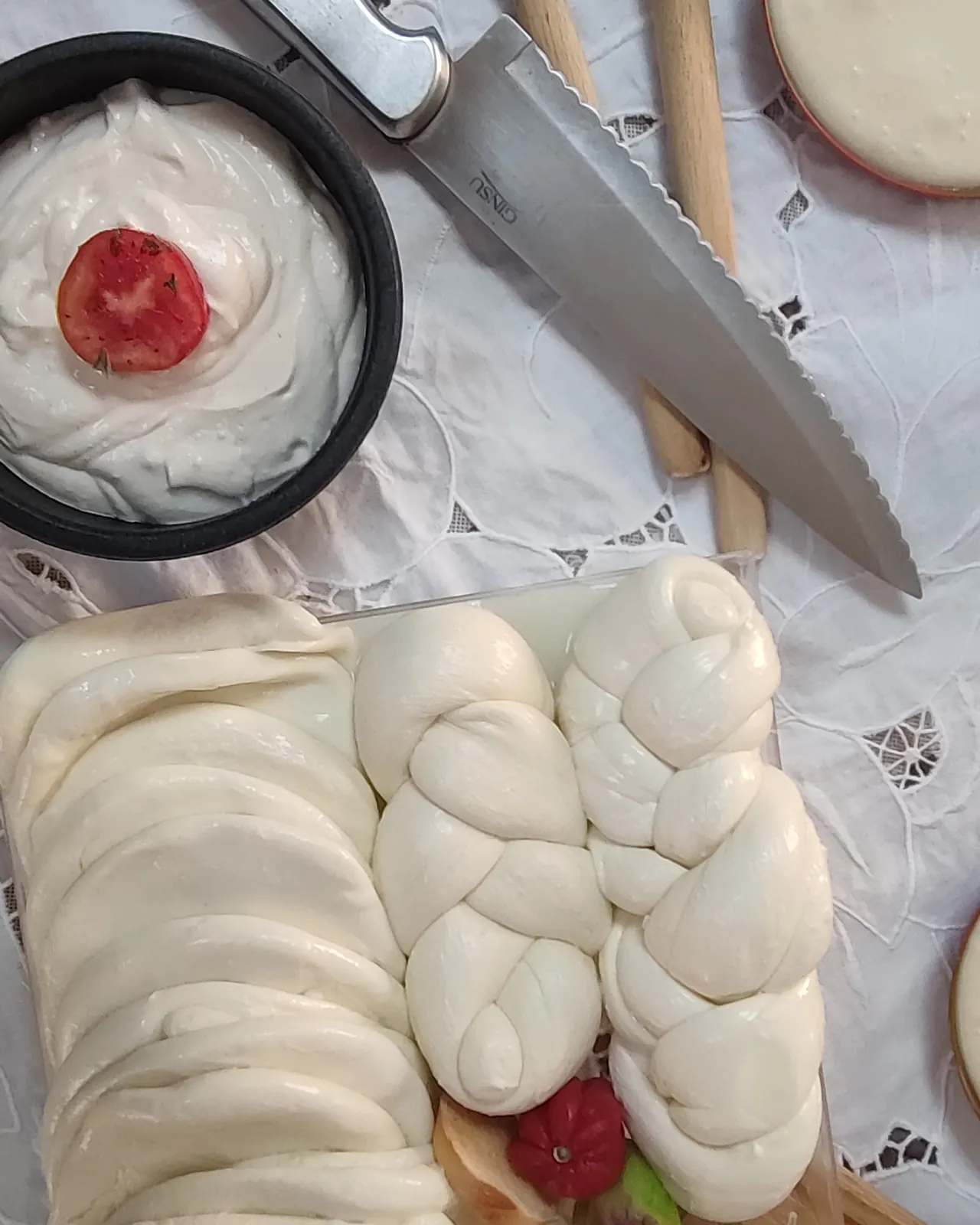 Queso trenza sobre una tabla junto a un cuchillo y un recipiente de yogurt